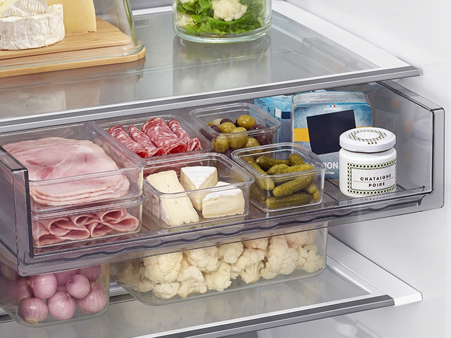 Multiple food containers are arranged on the refrigerator’s multi tray. As the tray moves downward, tall bottles from the lower section are repositioned to the top shelf.
