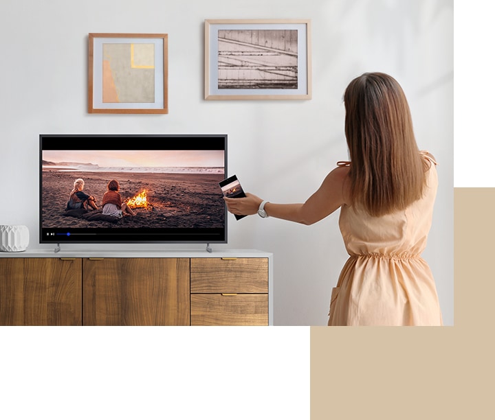 A woman is tapping mobile to TV which is on the drawer.