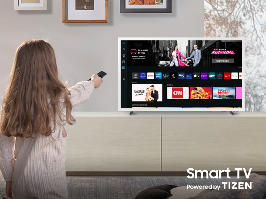 ⠀A girl is pointing the remote towards The Frame, which shows the Smart Hub home screen.