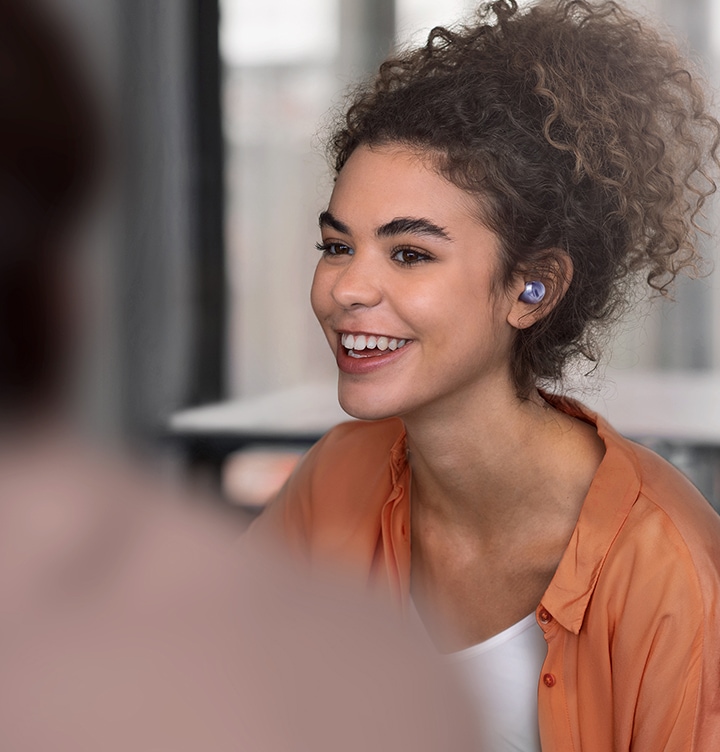 Une femme portant des Galaxy Buds Pro dans un café, parlant avec quelqu'un devant elle.