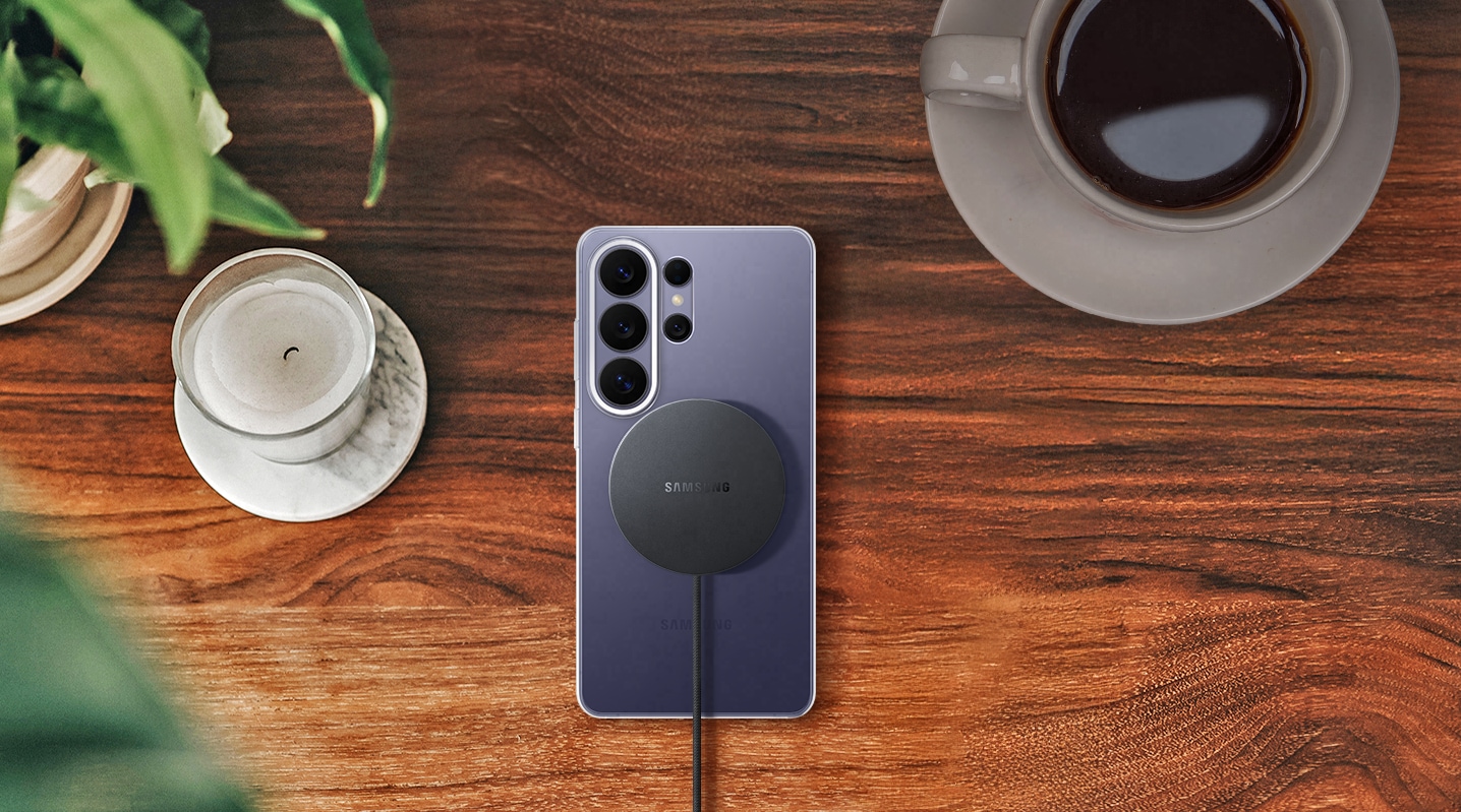 Top-down view of a Galaxy S26 Ultra in Cobalt Violet on a wooden surface in the Clear Magnet Case with the Magnet Wireless Charger aligned on the back, highlighting effortless charging.