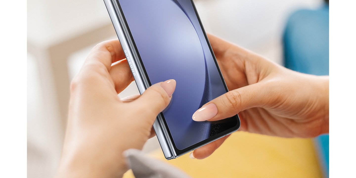 Hình ảnh hiển thị là hai tay cầm thiết bị Galaxy Z Fold5 sử dụng Miếng dán Màn hình và móng tay đang cứa vào màn hình để làm nổi bật lớp phủ chống trầy xước.