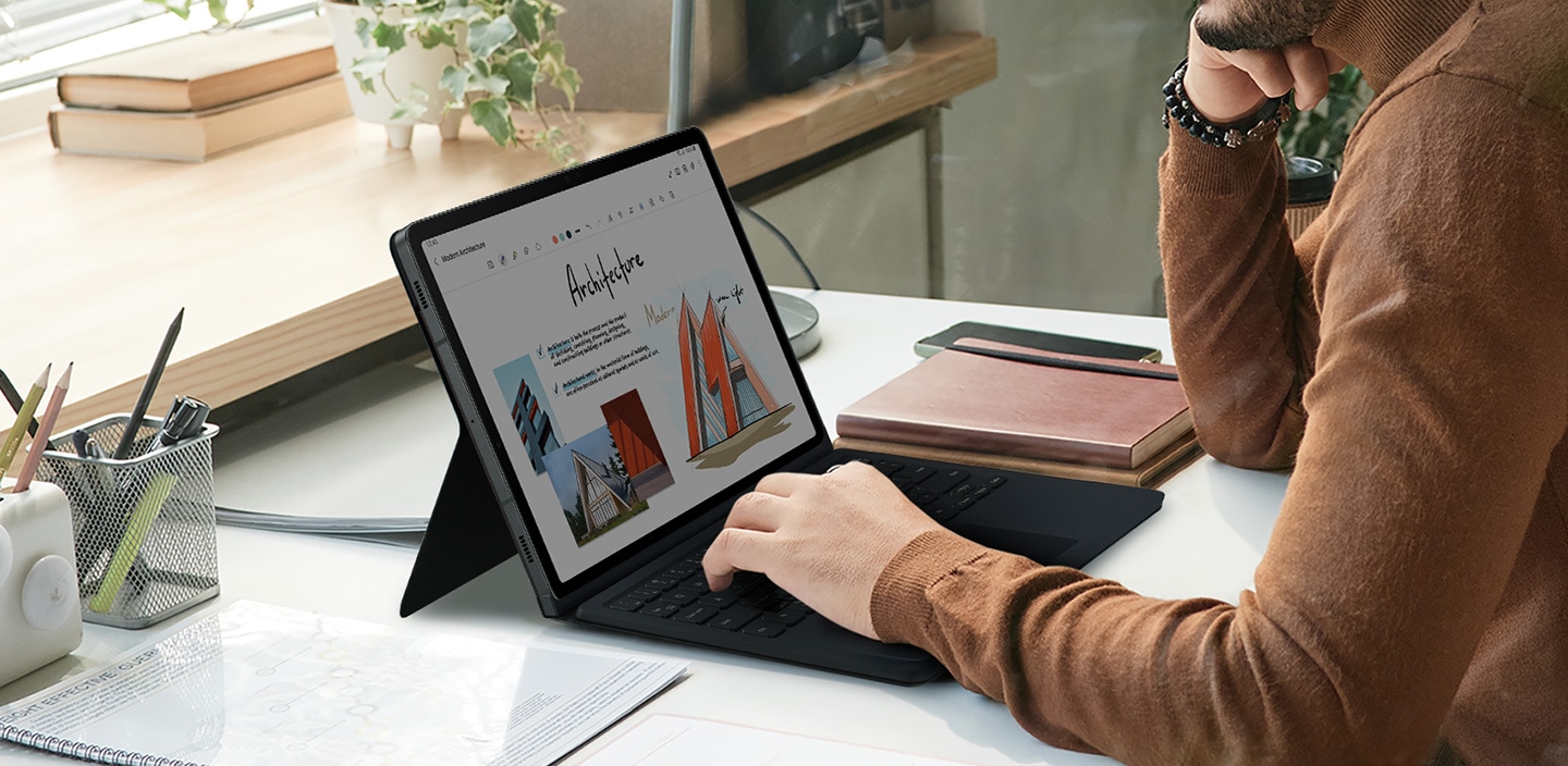 Một người đàn ông đang sử dụng Galaxy Tab S9 với bàn tay đặt trên bàn phím của Book Cover Keyboard.