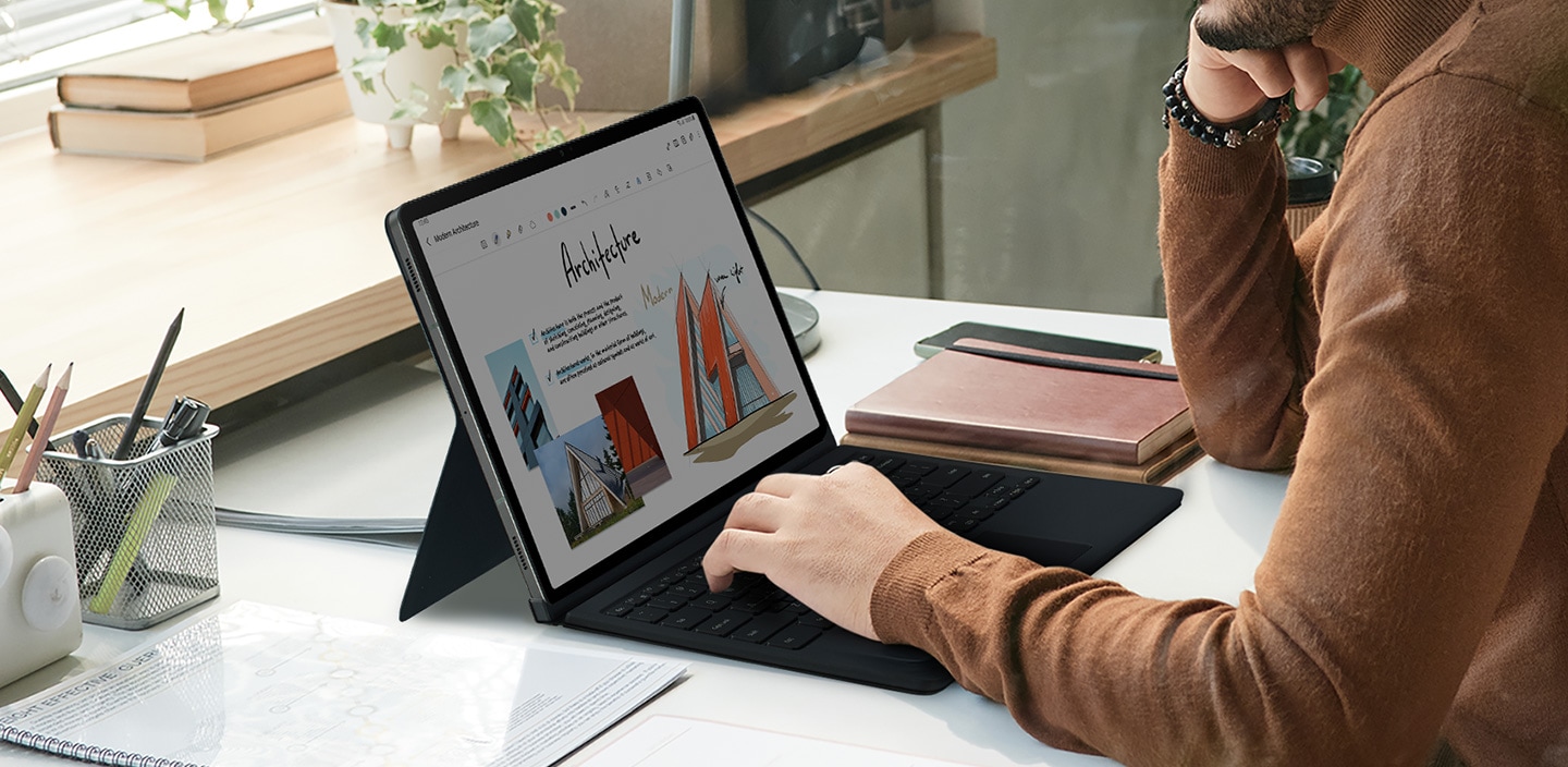 Một người đàn ông đang sử dụng Galaxy Tab S9+ với bàn tay đặt trên bàn phím của Book Cover Keyboard.