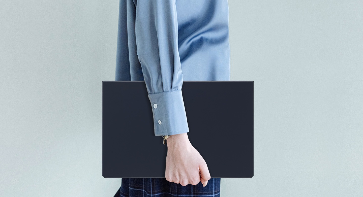 Một người mặc áo sơ mi màu xanh dương đang đi bộ trong khi cầm một chiếc Galaxy Tab S9 Ultra đang sử dụng Book Cover Keyboard Slim.