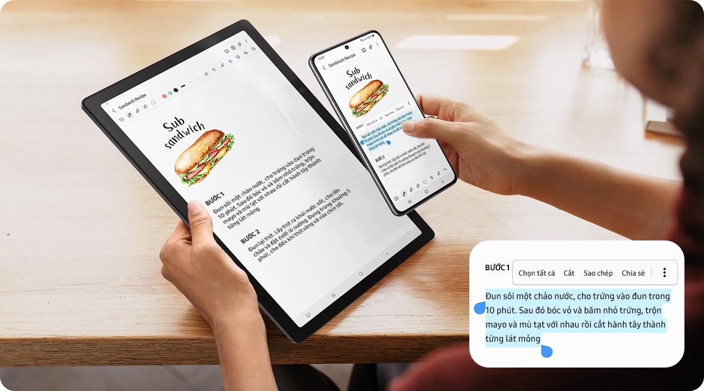 Một người đang cầm Galaxy Tab A8 bằng một tay và tay kia là điện thoại thông minh Galaxy. Một khối văn bản trên màn hình điện thoại được hiển thị đã chọn, theo đó các tùy chọn sao chép và dán được cung cấp.