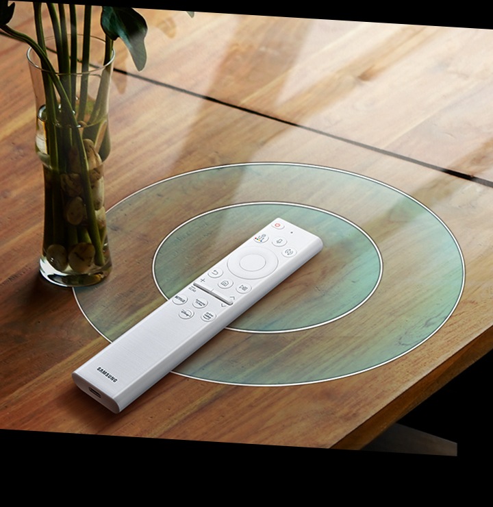 A SolarCell Remote is on a table being charged via the sun and nearby electronic devices.