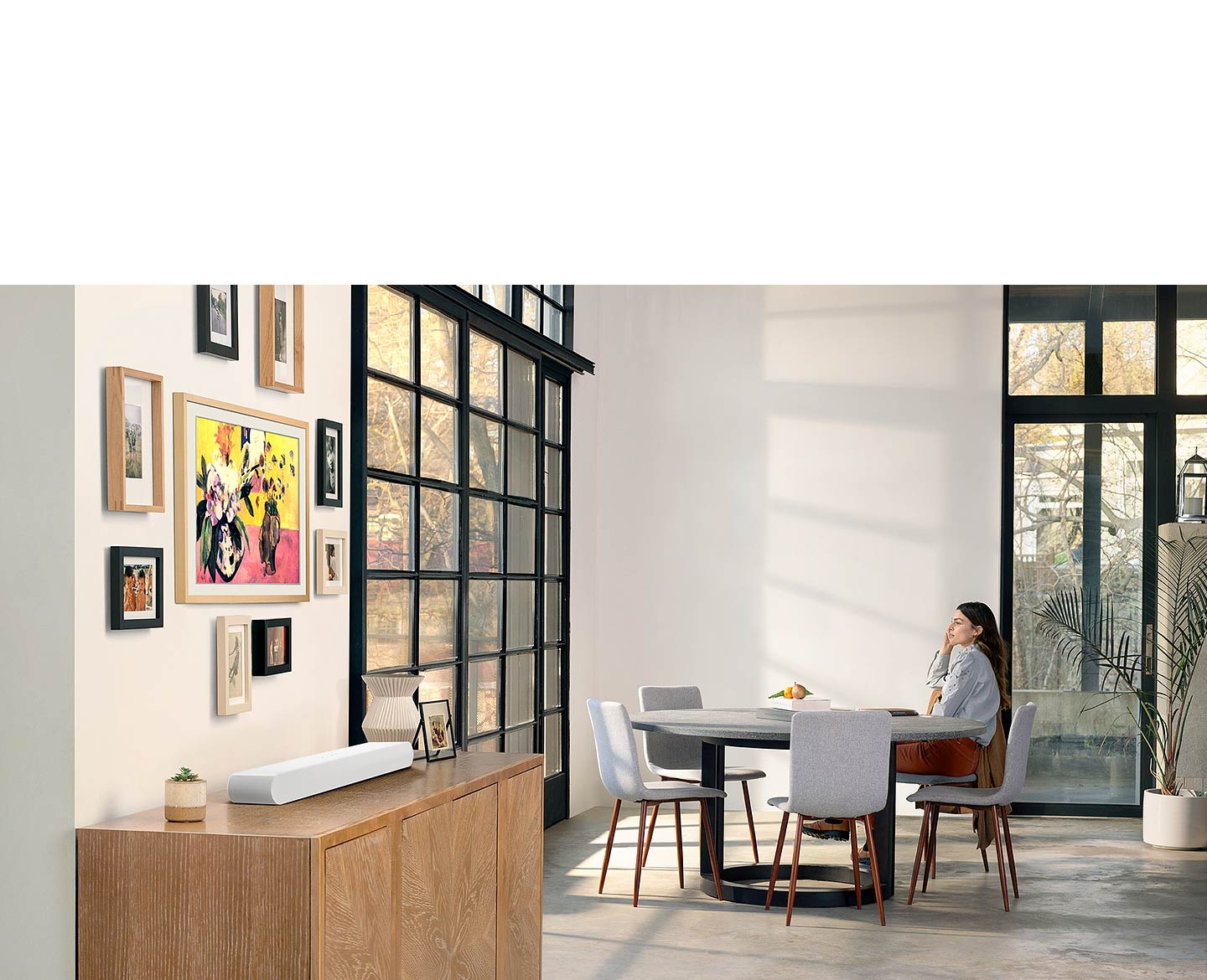 All-in-one design of S61B soundbar blends elegantly with living room interior as a woman sits at the table and looks out the window.