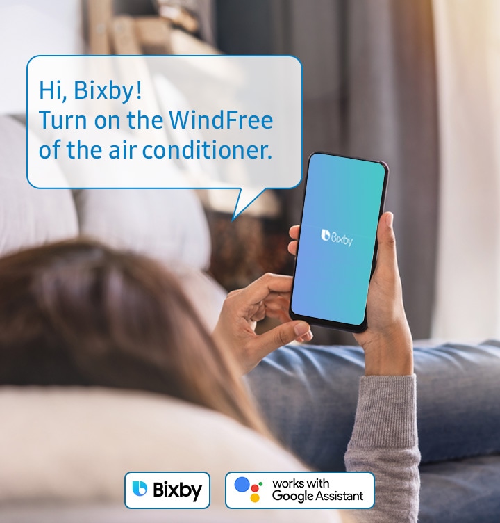 -Shows a person relaxing while controlling the air conditioning with their voice using a voice assistant on their smartphone, such as Samsung Bixby, Amazon Alexa or Google Assistant. The example voice command shown says: "Hi, Bixby! Turn on the wind free of the air conditioner."