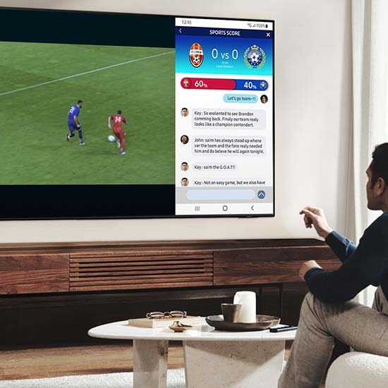 A man is watching a soccer game on his TV while simultaneously reading the news on the same screen.