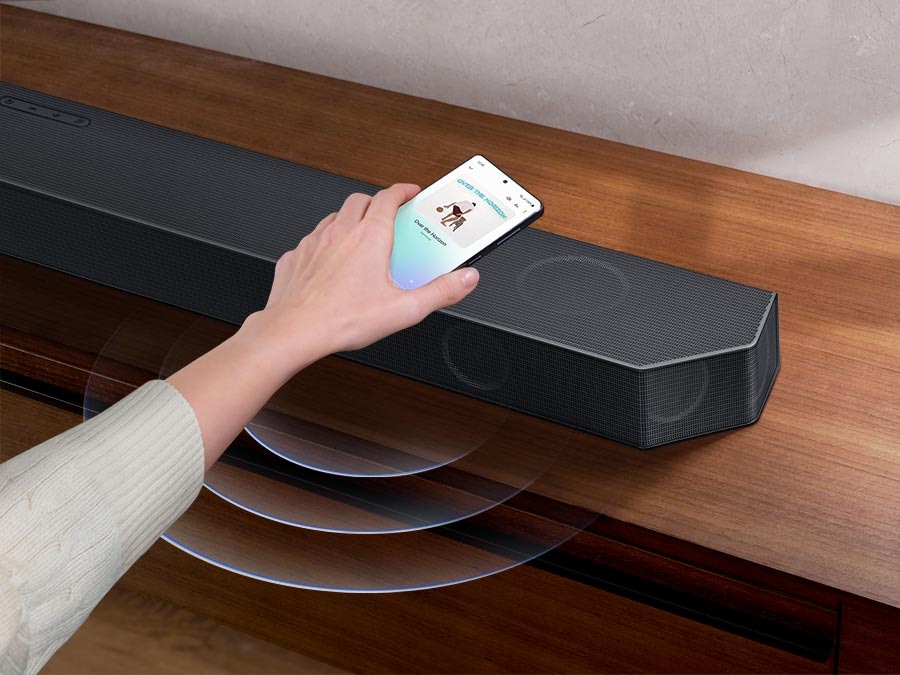 A hand taps a smartphone with the Samsung music app on-screen on the Soundbar. It instantly plays music, showing how easy it is to switch from smartphone to Soundbar.