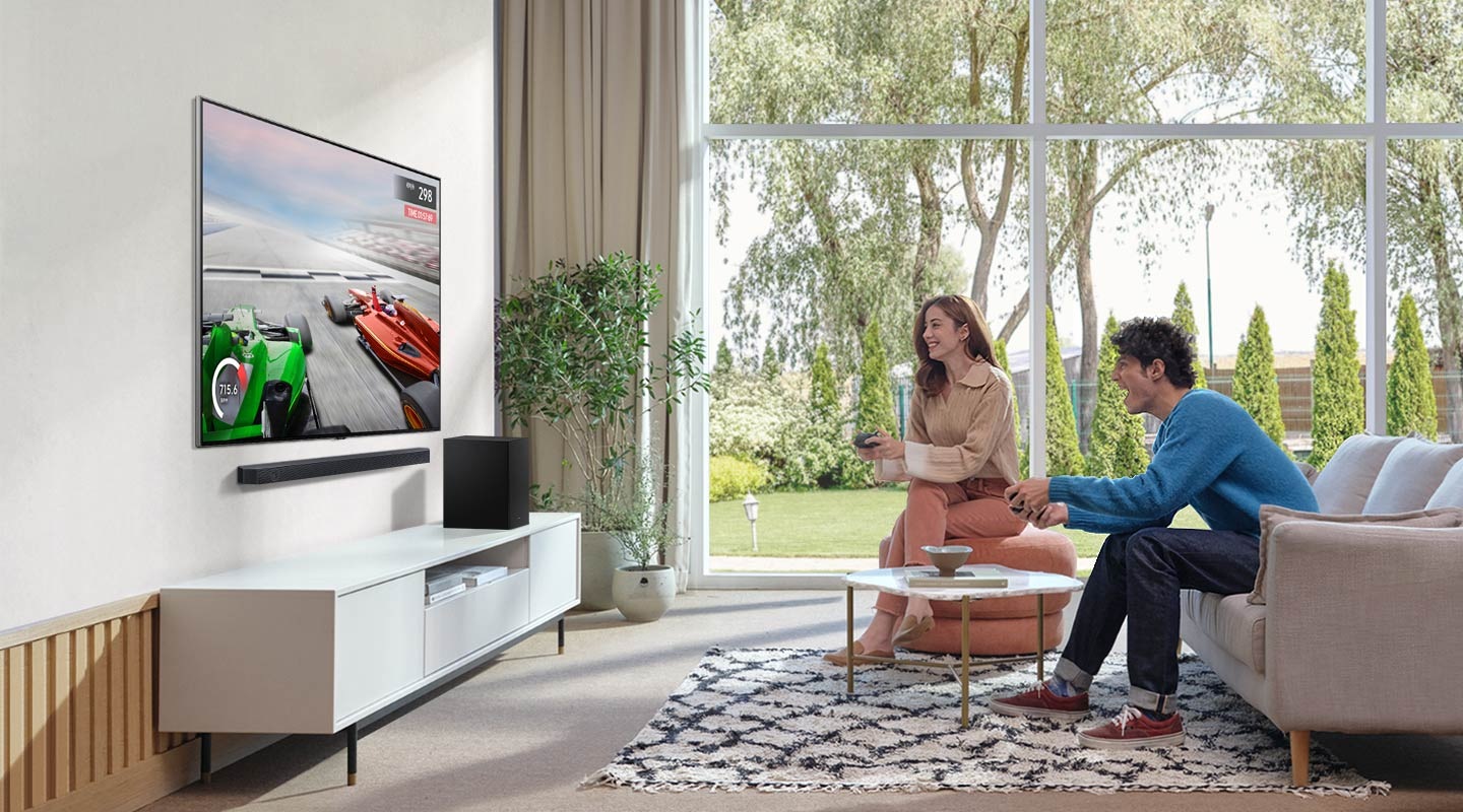 A man and woman enjoy the Soundbar’s Game Mode while playing a racing game on their TV connected to Soundbar and subwoofer.