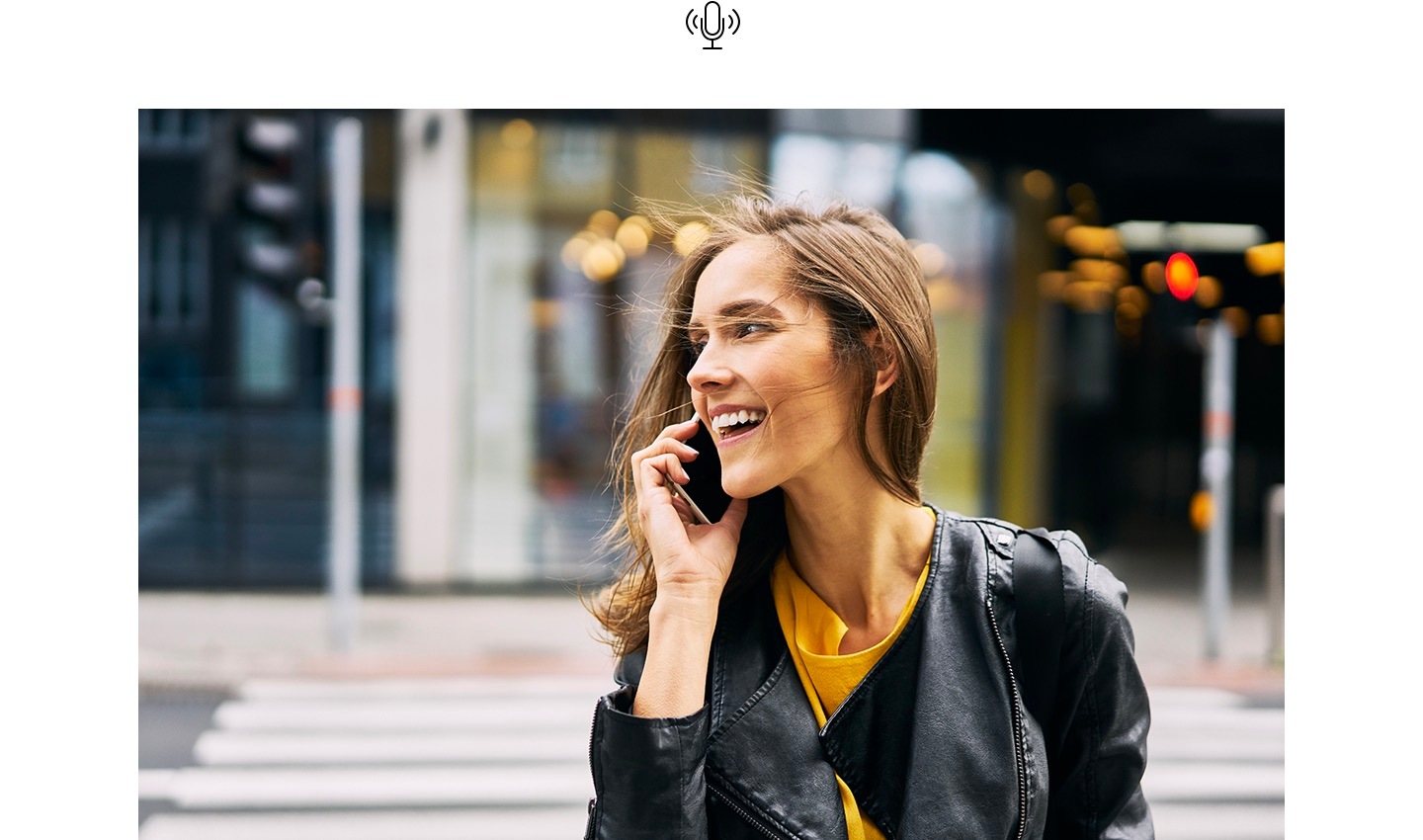 A woman, smiling, is talking on the phone while walking across the road. Above, the Voice Focus icon is shown.