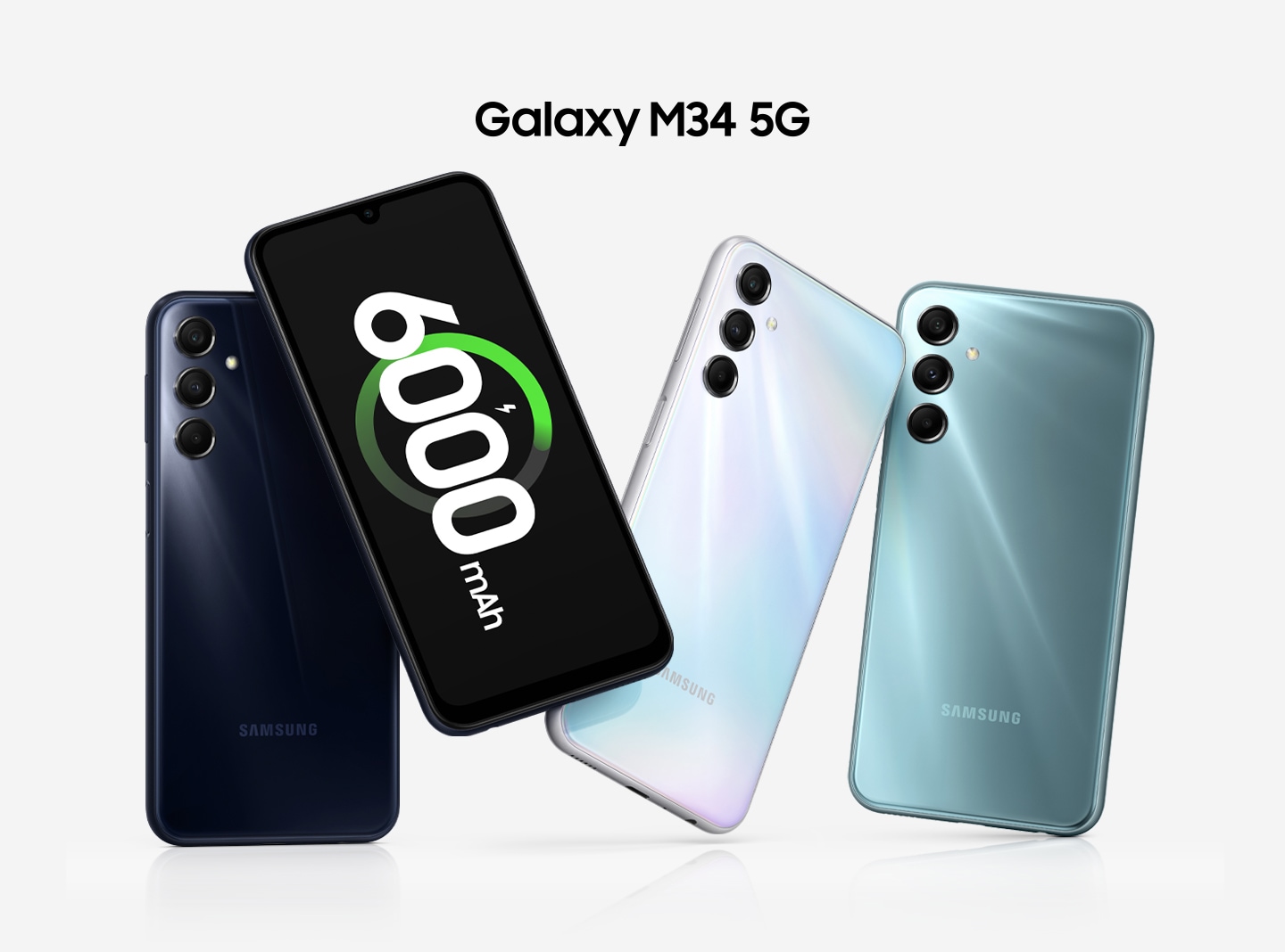 Four Galaxy M34 5G are shown together. At the very left, a Dark Blue Galaxy M34 5G’s back cover is shown. To its right, a frontal view is shown with the battery charging icon and the '6000mAh' shown on-screen. Then, the back covers of the Silver and Blue devices are shown.