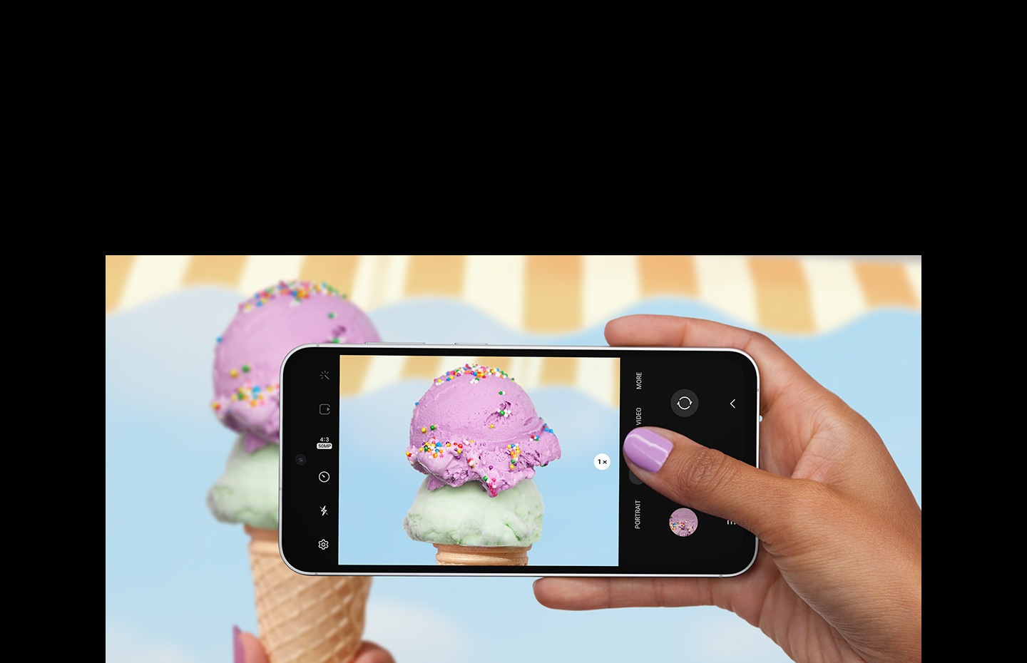 A hand taking a picture with a Galaxy S23 FE device seen from the front and horizontal. The screen in picture mode shows a clear and detailed picture of an up-close ice cream scoop with colorful sprinkles.