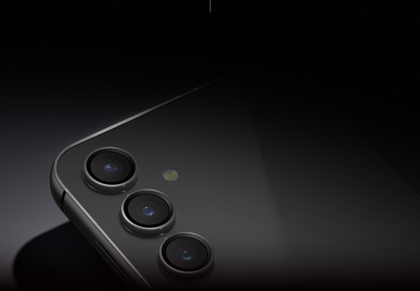 Một thiết bị Galaxy S23 FE màu xám Graphite nằm úp để hiển thị camera sau trong ánh sáng mờ.