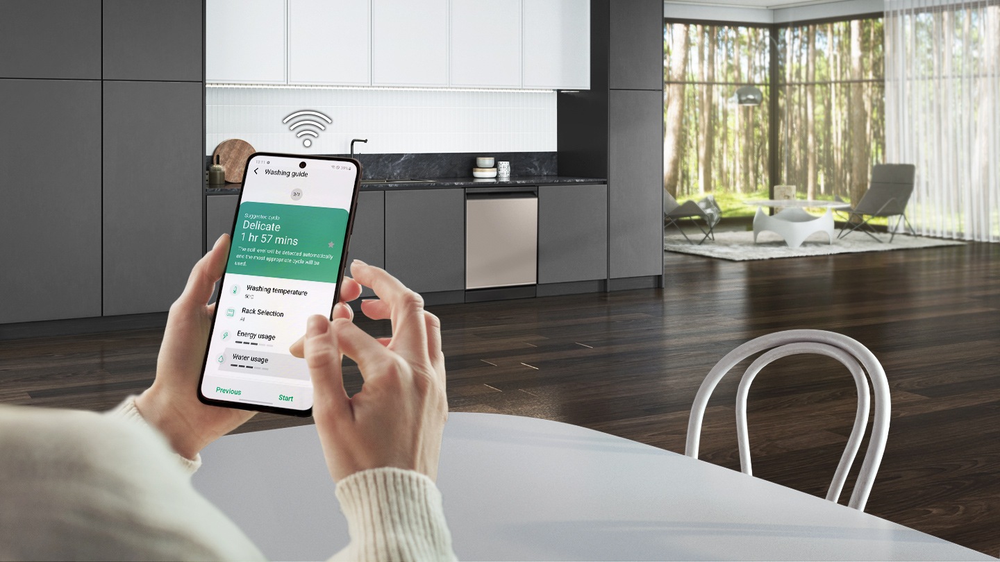 Hình ảnh một người đang ngồi trong căn bếp hiện đại đang sử dụng Ứng dụng SmartThings trên điện thoại thông minh để theo dõi và kiểm soát hiệu suất của máy rửa bát. Màn hình hiển thị Hướng dẫn Giặt, với chu trình và thời gian giặt được đề xuất cũng như nhiệt độ giặt, lựa chọn giá đỡ cũng như mức sử dụng năng lượng và nước.