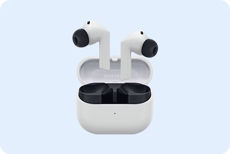Hình ảnh minh họa một cặp tai nghe Samsung Galaxy Buds3 FE màu trắng với nút tai màu đen được đặt trong hộp sạc màu trắng mở. Hộp sạc mở, để lộ các khe cắm tai nghe bên trong để sạc.