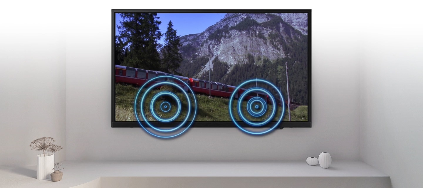 Màn hình TV hiển thị cảnh một đoàn tàu chạy ngang qua một khung cảnh ngoài trời đẹp mắt. Khi tàu chạy qua, sóng âm xuất hiện gần nơi tàu chạm vào đường ray, cho thấy tiếng ồn trong cảnh quay.