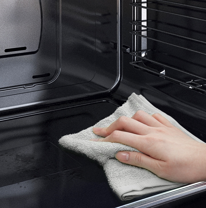 A person is wiping down the ovenâs Easy Clean surface using just a cloth.