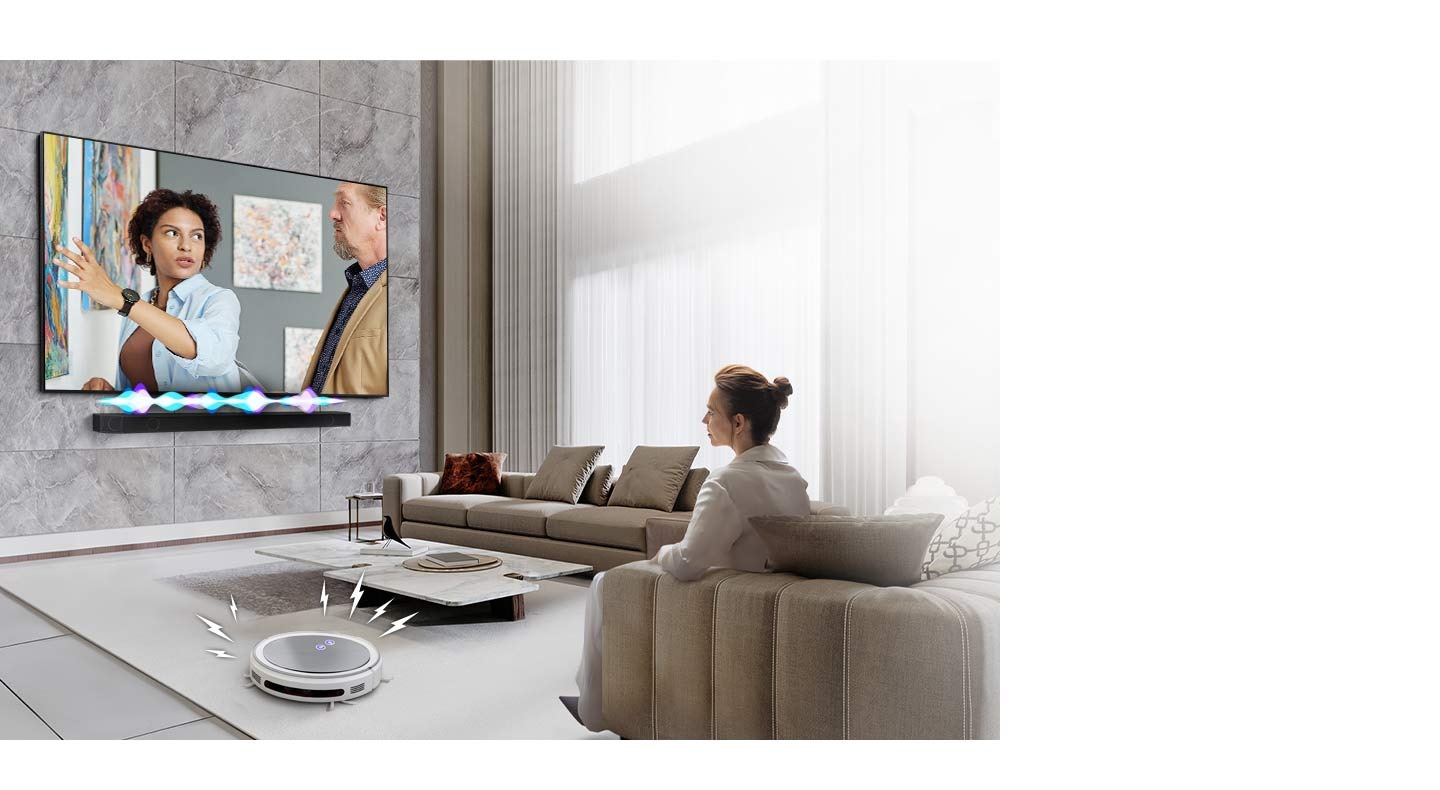 A woman is watching TV, which has a Soundbar installed directly underneath. The Soundbar has an audio bar indicating the level of volume. A robot vacuum cleaner rolls into the room, giving off distracting noise indicated by lighting bolts. In response, the Soundbar plays at a louder volume, with the audio bar giving off greater activity.