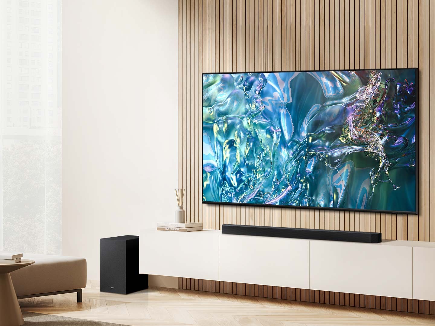 A wide-screen TV displays a blue wavelike pattern on screen. Underneath is a Soundbar, with a subwoofer to the side.