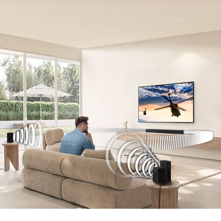 A man watches TV. A Soundbar and rear speakers give off sound waves of different types traveling toward the man.