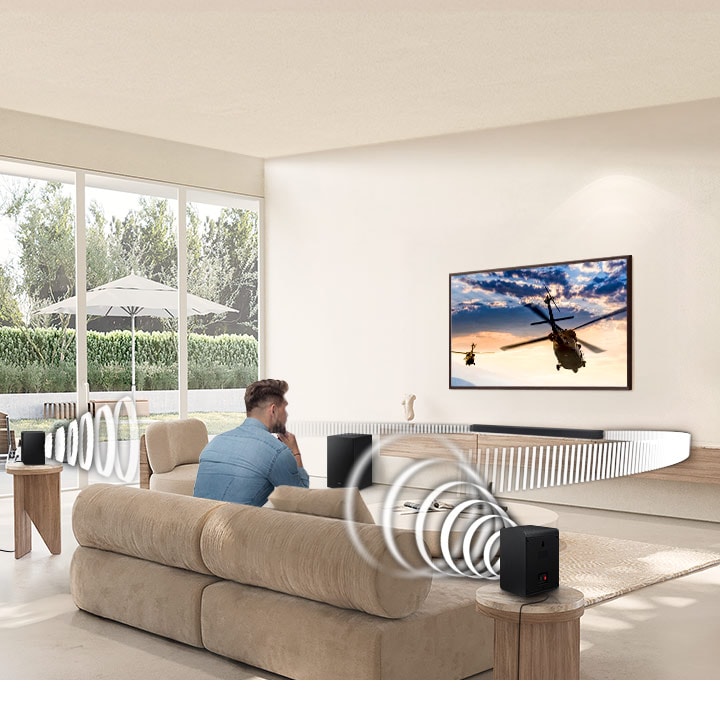 A man watches TV. A Soundbar and rear speakers give off sound waves of various types, traveling in different directions.