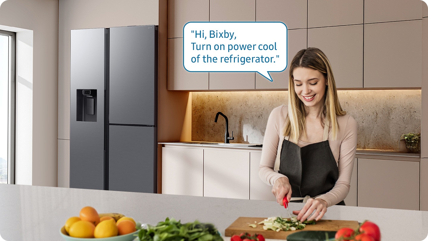 Shows a person preparing food while controlling the refrigerator using a Samsung Bixby. “Hi Bixby, Please update the status of other devices.”