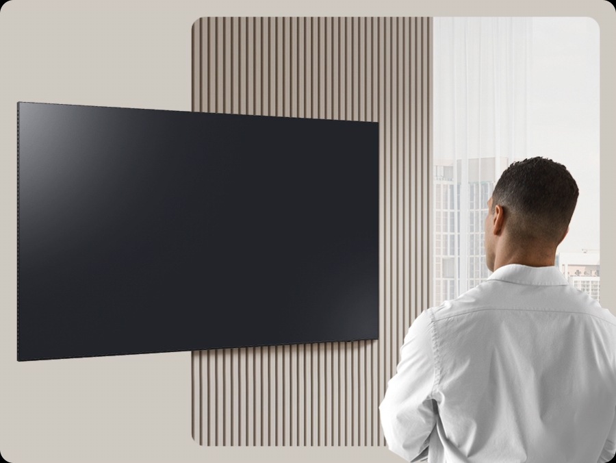 A man looks at a blank TV screen. The screen activates to display Daily Board, which shuffles through widgets for Weather, Memo, Music, Home Stats, Samsung TV Plus and Tips. It also displays the time and date, along with a voice prompt to play relaxing music.