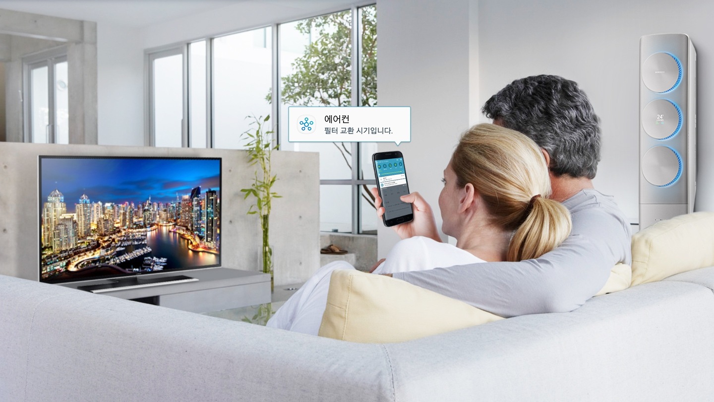 남자, 여자가 함께 소파에 앉아 TV를 보던 중 스마트폰에서 