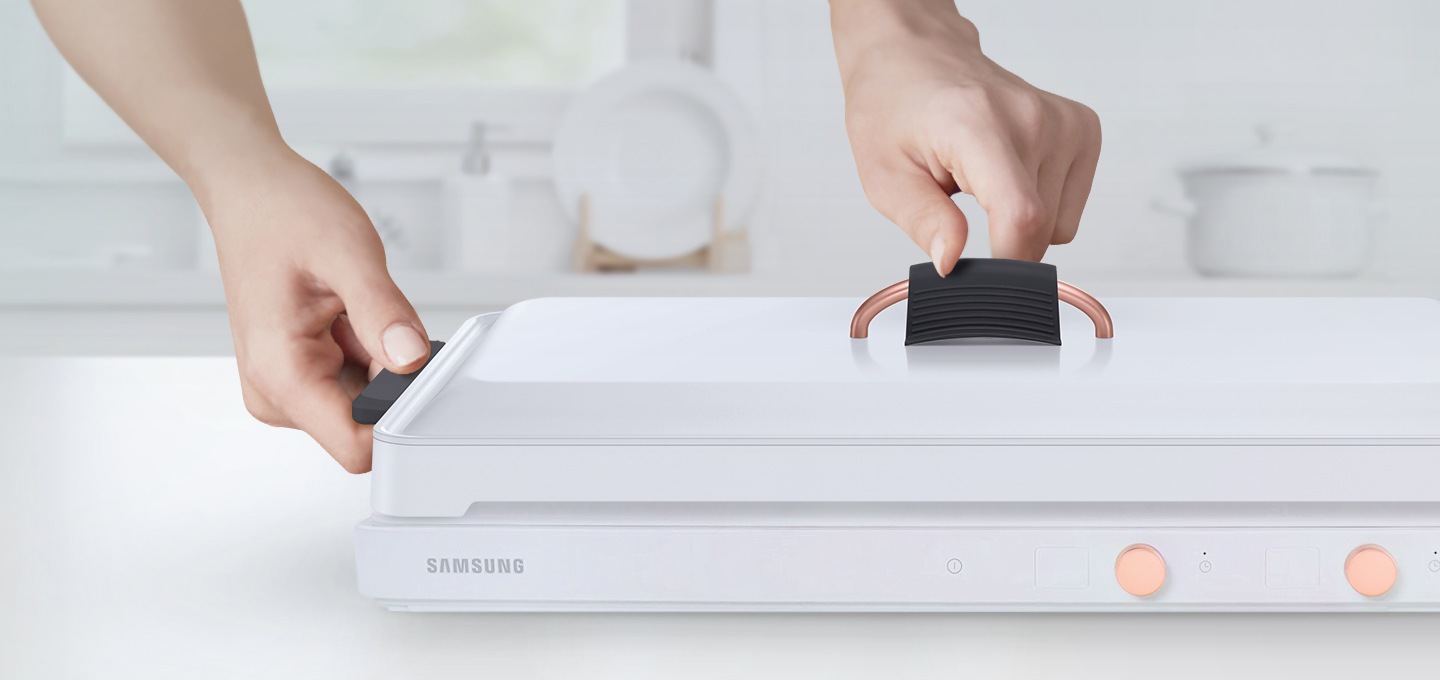 테이블위에 놓인 전용용기에 좌,우측 실리콘 손잡이와 뚜껑 실리콘 손잡이가 결합되어 있고 손으로 뚜껑을 잡는 모습이 보여집니다.