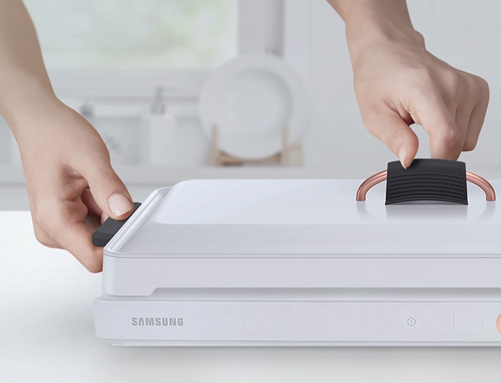 테이블위에 놓인 전용용기에 좌,우측 실리콘 손잡이와 뚜껑 실리콘 손잡이가 결합되어 있고 손으로 뚜껑을 잡는 모습이 보여집니다.