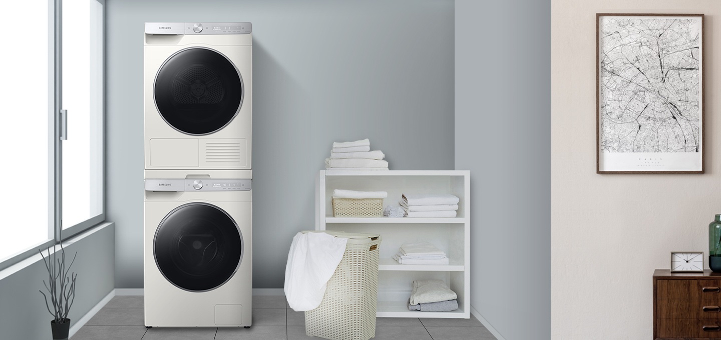 [블루톤 벽지의 다용도실 인테리어 컷입니다. 좌측에 창문이 있고 화이트 색상 세탁기/건조기가 직렬 설치되어있습니다. 세탁기/건조기 우측에는 라탄 바구니와 수납장이 있으며 하얀 수건이 보관되어 있습니다. 이미지 우측에는 액자가 걸려있는 벽면입니다.]