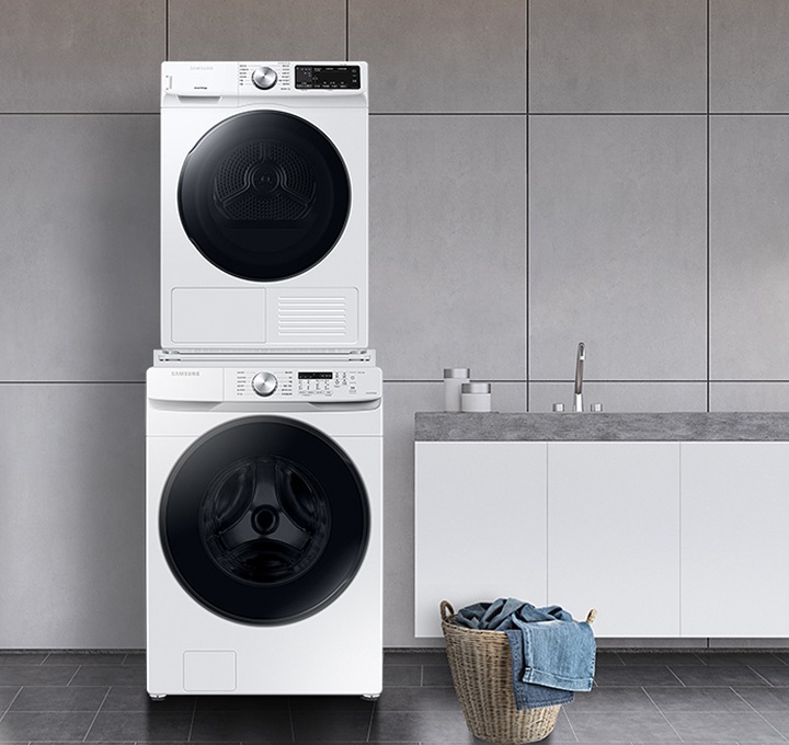 [그레이 타일로 인테리어 되어있는 넓은 다용도실이 보이며, 좌측엔 비스포크 그랑데 ÁÍ 세탁기 건조기가 건조기 상단키트를 사용해 하나로 되어 있는 모습이 보이며, 가운데에 수납공간이 하단에 함께있는 세면대가 보이며 세면대 위 좌측엔 세탁세제 통이 보이고 우측엔 개어져 있는 하얀색 수건 6개가 보여지고 수건 우측엔 작은 흰 화분이 보여집니다. 세면대 앞엔 라탄의 빨래통과 안에 청바지 빨래가 들어있으며, 우측엔 사다리가 있으며 사딜에 상단에 수건이 걸려있고 두번째 칸에 수건이 개어져 있습니다.]