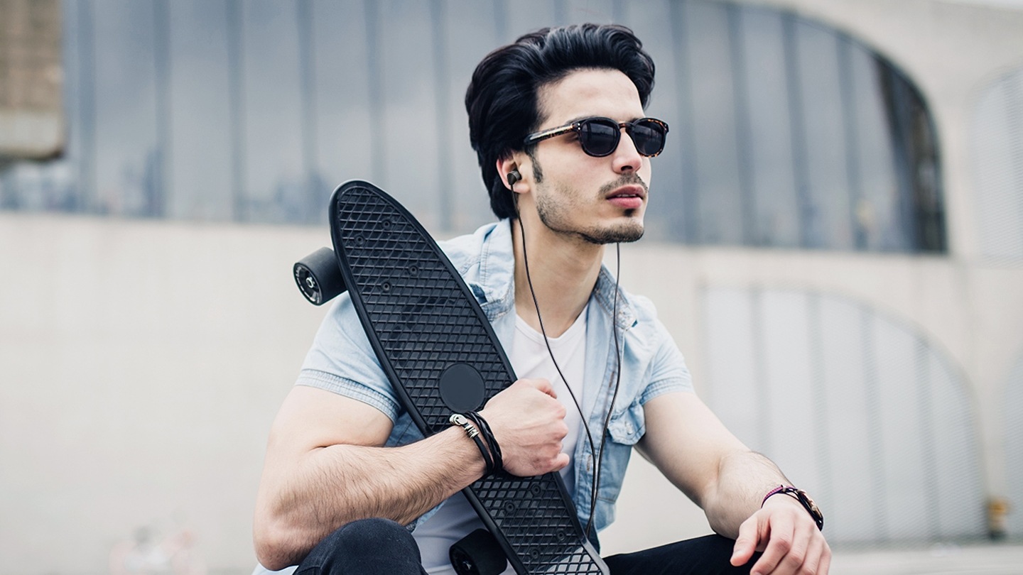 보드를 가지고 앉아있는 남자의 모습이 보입니다. 귀에는 블랙 제품을 착용하고 있는 모습입니다. 