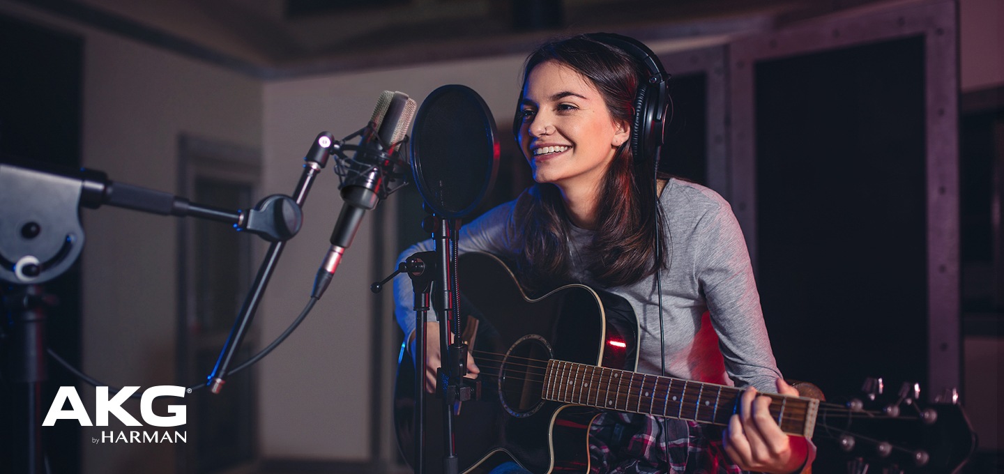 여성이 기타를 들고 마이크 앞에서 작업을 하고 있습니다.