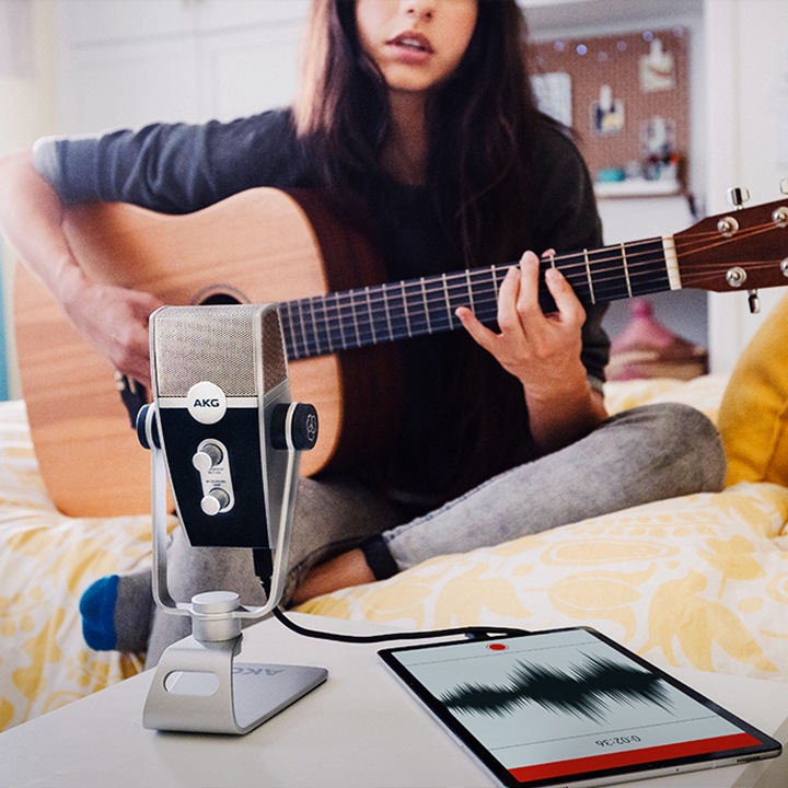 여성이 기타를 연주하며 마이크에 태블릿을 연결하여 녹음하고 있습니다.