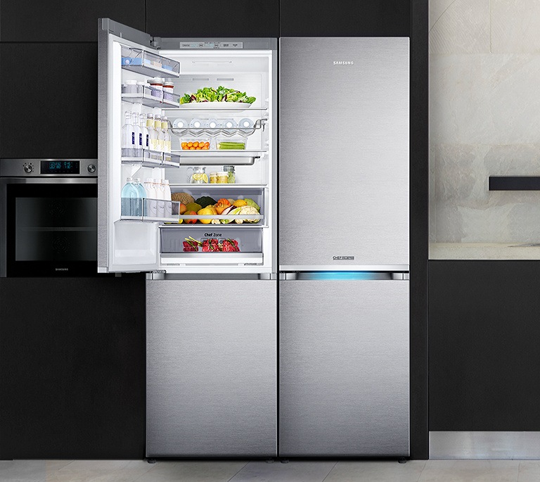 블랙/화이트톤 인테리어컷으로 오른쪽에 싱크대와 화구가 있는 인테리어컷 입니다. 왼쪽에는 블랙 컬러 냉장고장에 셰프 컬렉션 빌트인 냉장고 2대가 설치되어 있습니다. 2대의 냉장고 중 왼쪽 냉장고 상칸 도어가 오픈되어 있고 안에 음료와 각종 과일 및 식재료가 가득 차 있습니다.