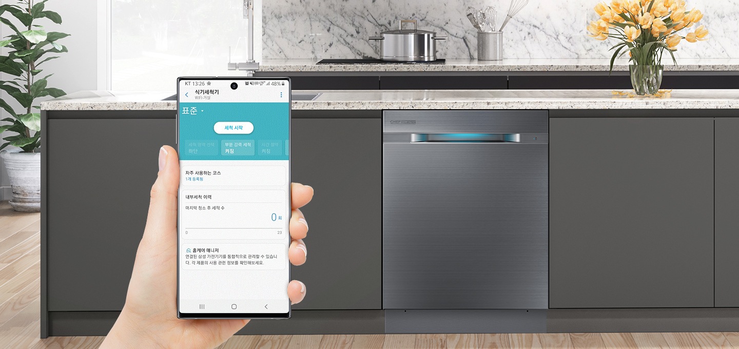 빌트인된 식기세척기가 배경으로 보여지며 손에 쥐고 있는 스마트폰 화면에는 스마트 컨트롤이 실행되고 있습니다.