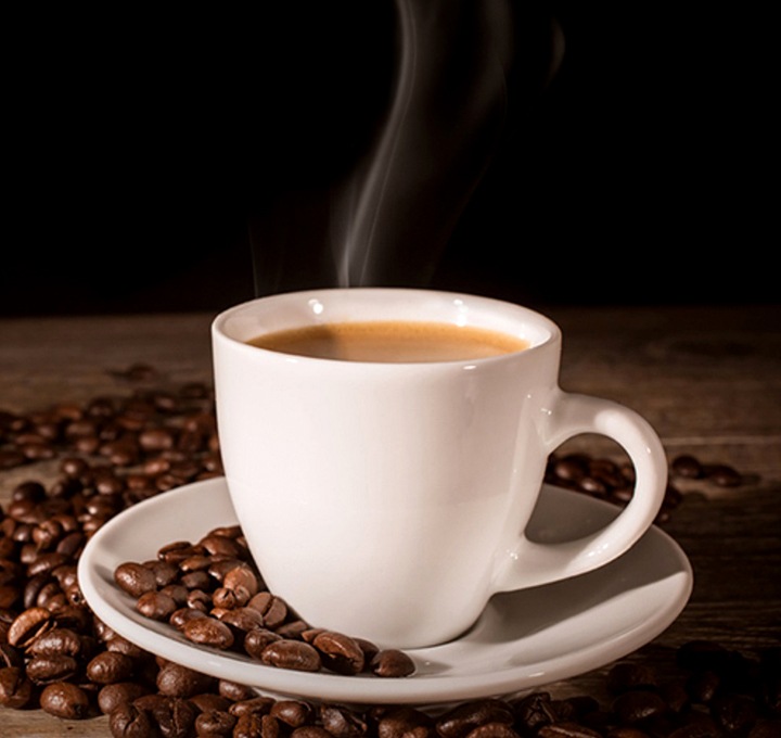 흰색 커피잔에 커피가 담겨있고 주변에 여러개의 커피 콩이 늘어져 있는 모습