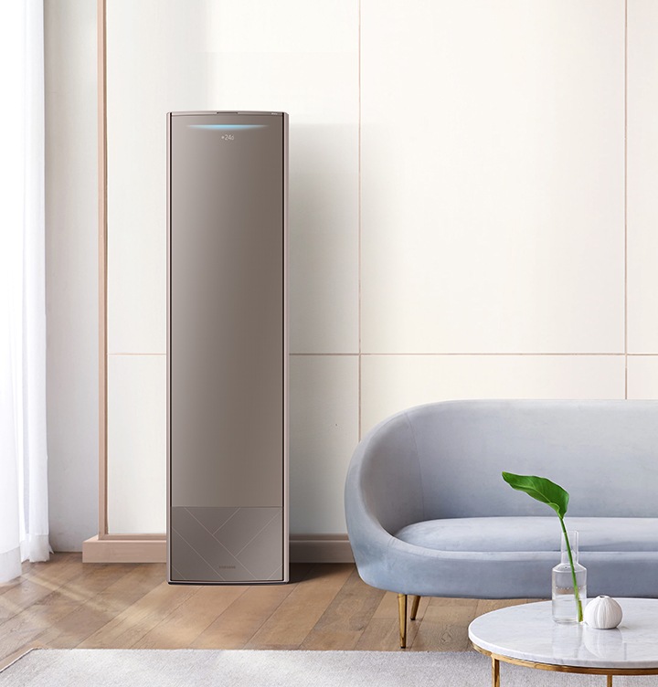 거실에 좌측에 설치된 에어컨이 작동하는 모습이 보여지며, 우측엔 블루계열의 쇼파와 앞에 탁자가 보여지며 탁자위에는 화병에 잎파리 가 보여집니다. 