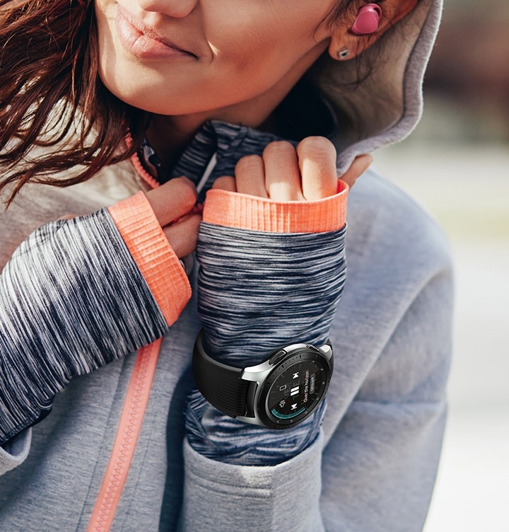 운동을 하는 여성의 손목에 갤럭시 워치가 착용되어 있으며, 기어 아이콘 X도 착용하고 있습니다.