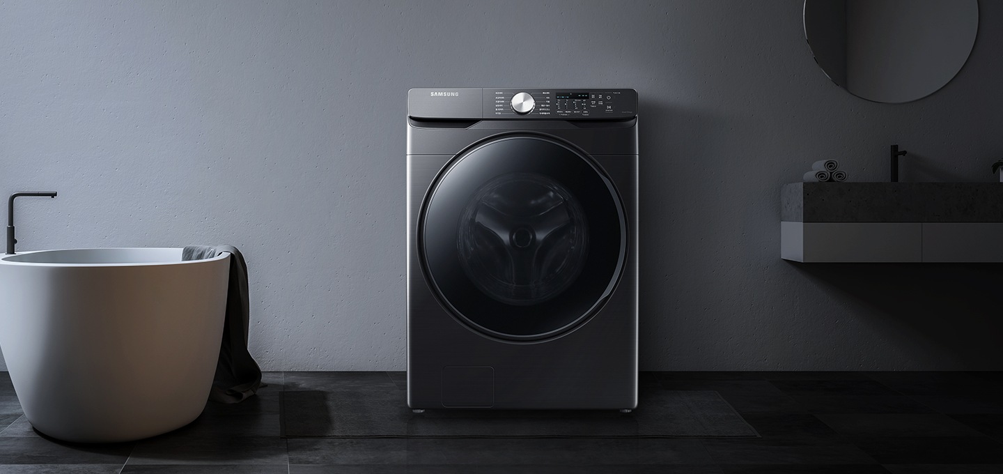 그레이톤의 욕실 공간에 삼성 그랑데 세탁기 제품이 놓여져 있습니다. 좌측에는 욕조가, 우측에는 세면대와 거울, 수건이 놓여져 있습니다.