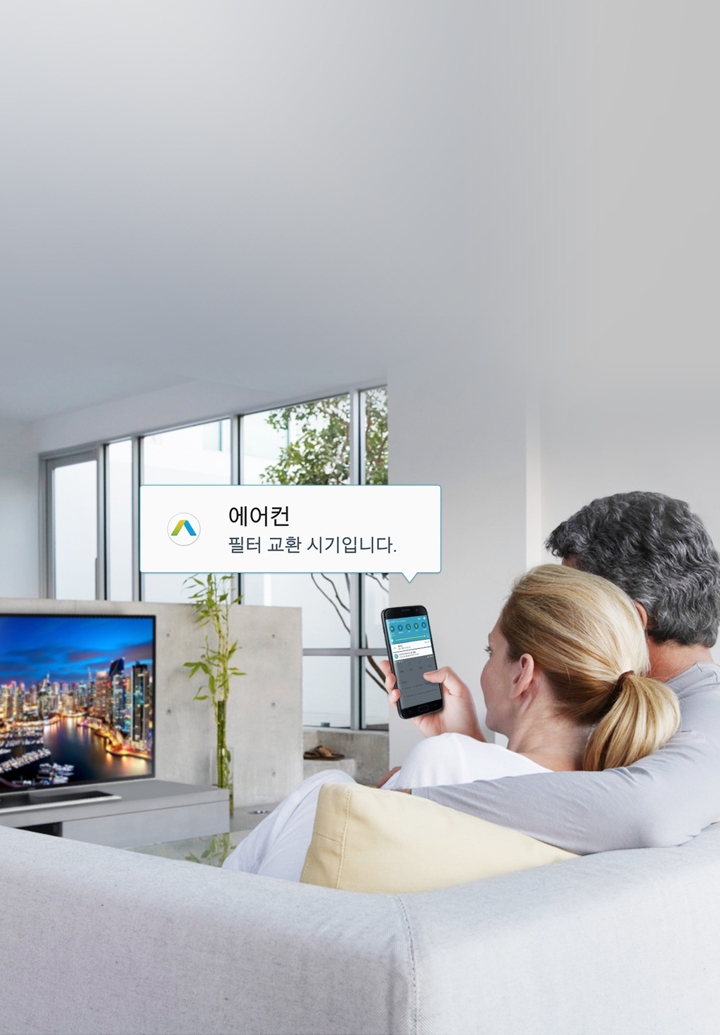 남자, 여자가 함께 소파에 앉아 TV를 보던 중 스마트폰에서 