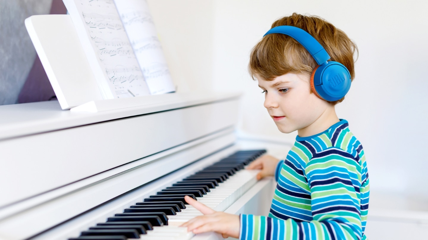 남자아이가 블루색상 헤드폰을 착용하고 피아노를 치고 있는 모습이 보입니다.