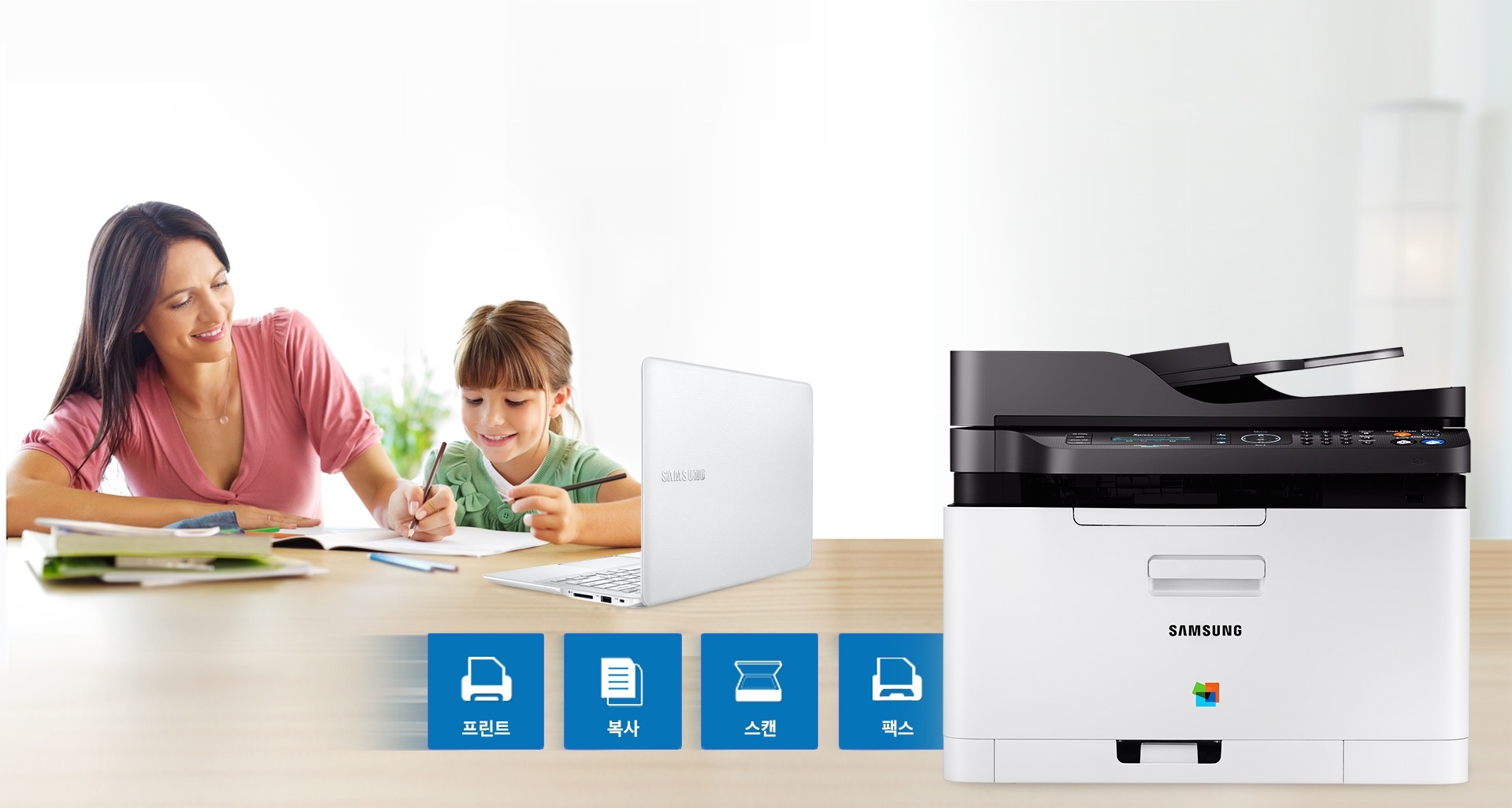 왼쪽에 성인여자와 어린여자아이가 책상위에 노트북을 올려놓고 있고, 오른쪽에 SL-C483FW제품과 인쇄,스캔,복사, 팩스 아이콘이 있다.