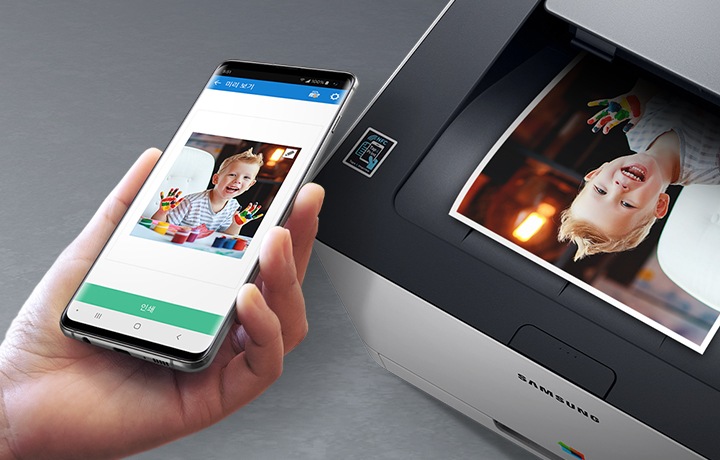 검정 색상의 나무 책상에 제품의 왼쪽 위에서 내려본 이미지가 있고 스마트폰을 제품 이미지 상단에 NFC 태그 스티커가 붙어있는 부분에 태그하는 이미지입니다.