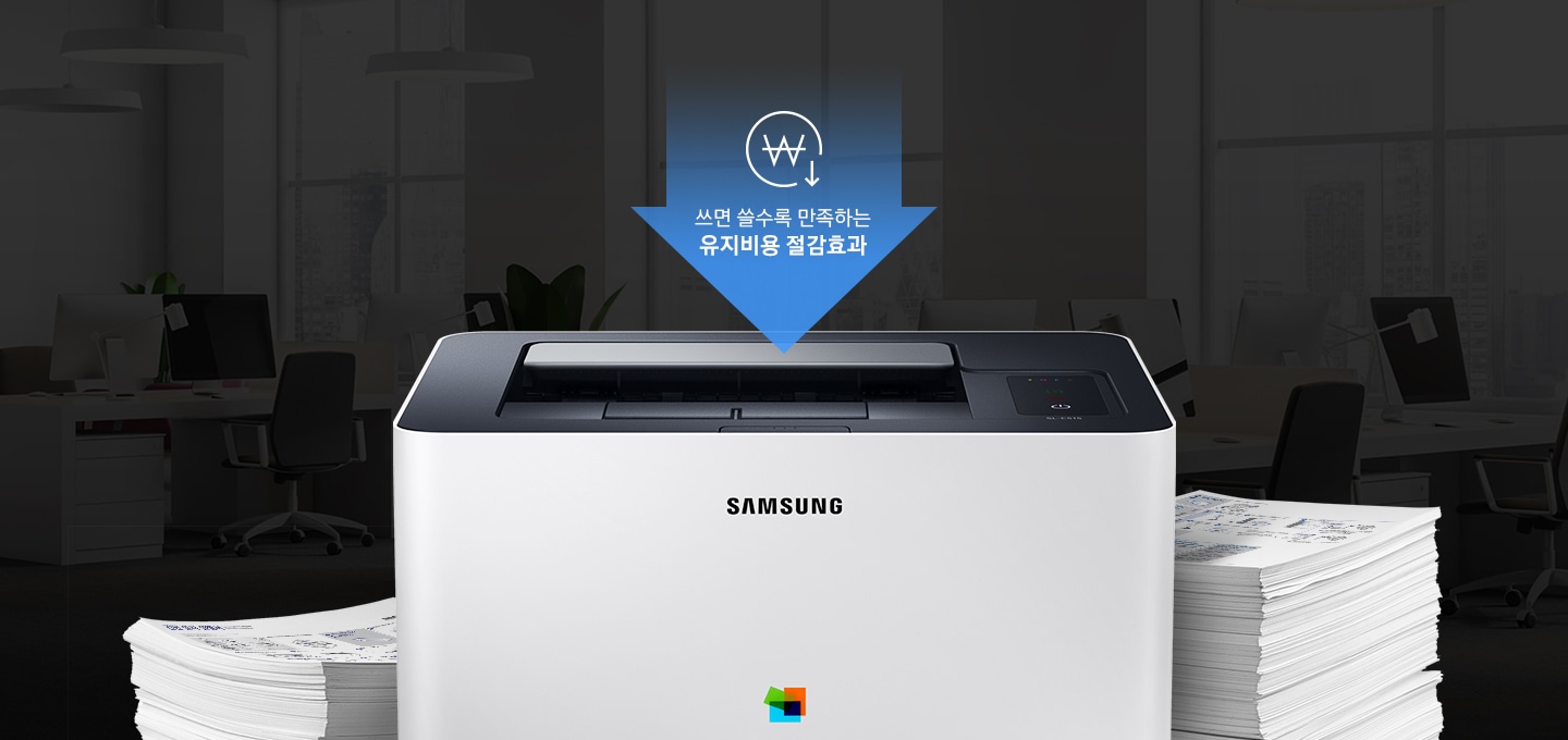 어두운 사무실 배경에 이미지 중간에는 제품 정면 이미지가 놓여있고 제품 이미지 양옆으로는 종이가 쌓여있습니다. 제품 이미지 상단에는 아래로 내려오는 파란 색상에 화살표와 화살표 안에 쓰면 쓸수록 만족하는 유지비용 절감효과 텍스트와 동그라미 안에 원 표시와 오른쪽 하단에 아래로 내려가는 아이콘이 있습니다.