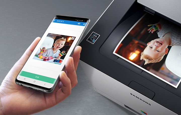 프린터에 NFC를 연결하여 스마트폰의 이미지를 출력 할 수 있음을 알려주는 이미지 입니다. 프린터 NFC라고 적힌 아이콘 위에 스마트폰을 들고 있고, 스마트폰 배경에는 아이의 사진이 있습니다. 제품 프린터에는 핸드폰에 있는 이미지와 동일한 이미지가 출력 되어있습니다.